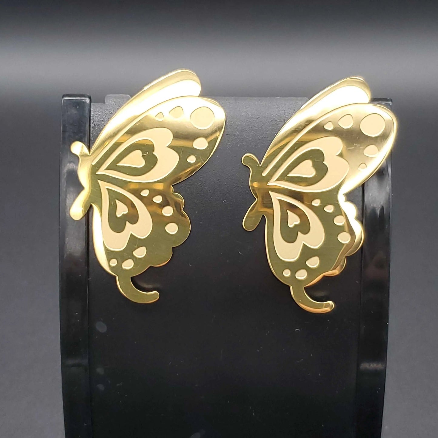 Gold butterfly earrings on a black stand against a dark background