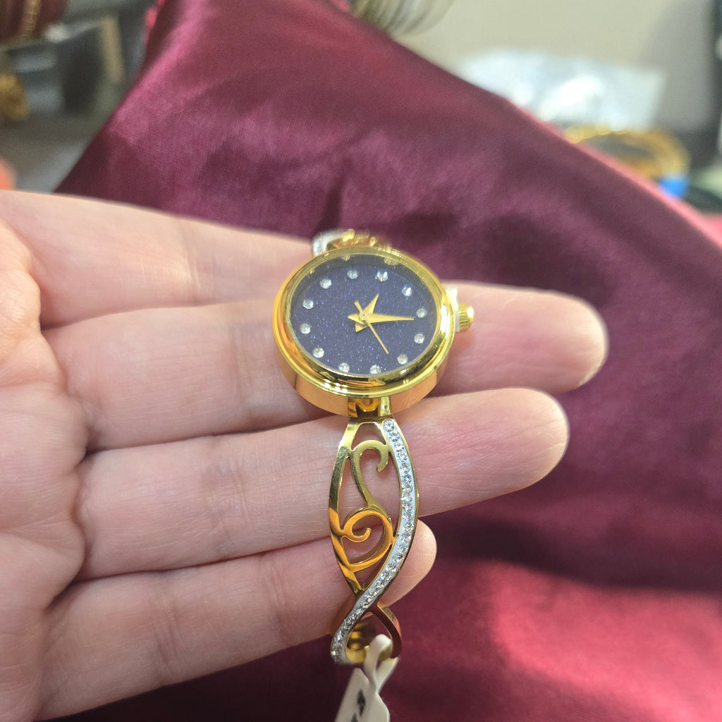 Gold watch with a black face held in a hand against a maroon fabric background