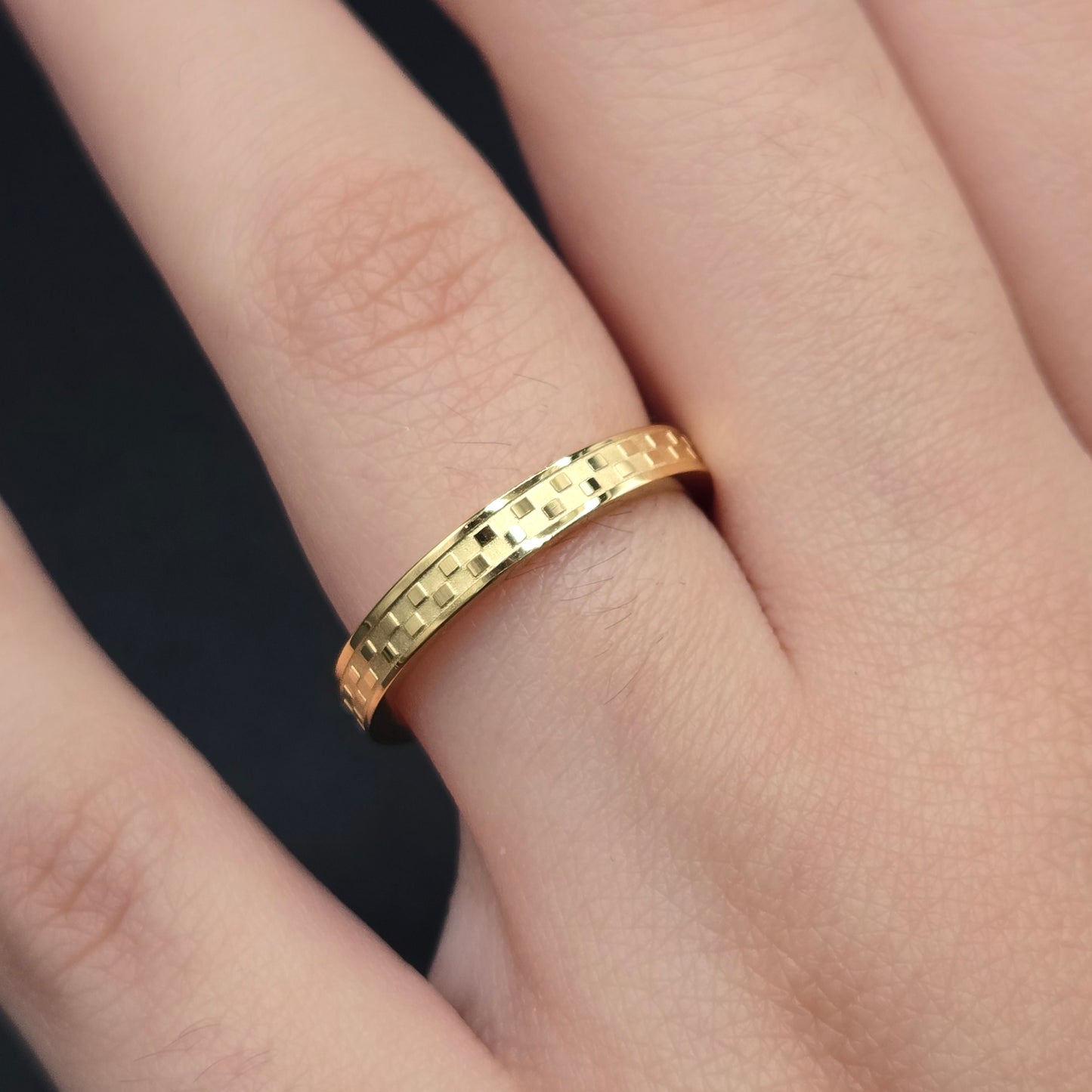 A gold-colored stainless steel Chess ring on a person's finger, displaying a laser engraved pattern.