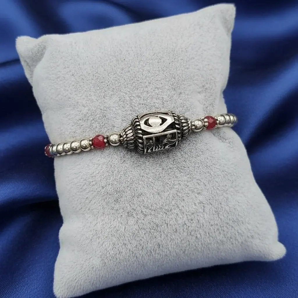 evil eye bracelet made of sterling 925 silver with red beads on a gray cushion against a blue satin background