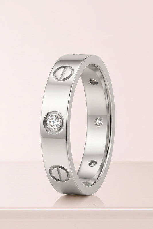 A yellow gold ring with screw details and a round-cut diamond in the center, displayed on a light pink background. Cartier Love Design