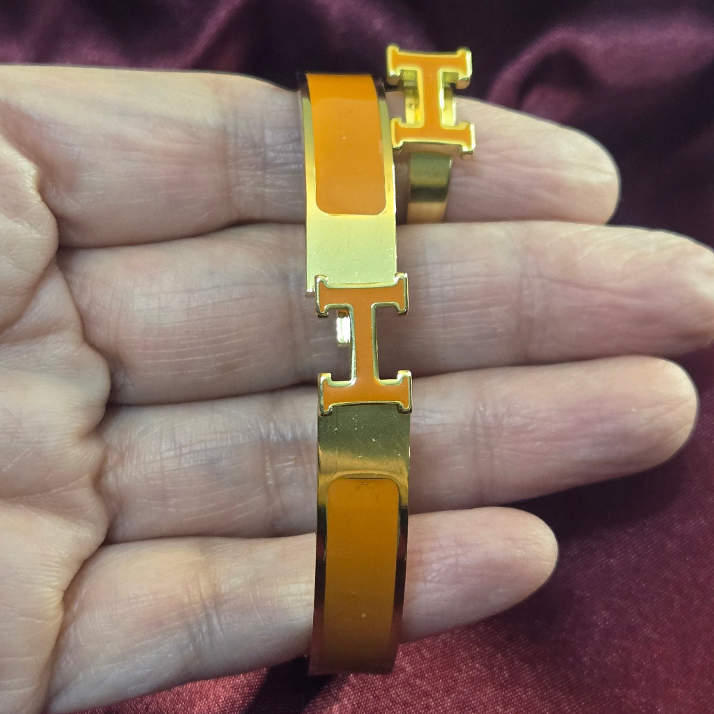 Gold bracelet with a distinctive clasp on a hand against a dark fabric background