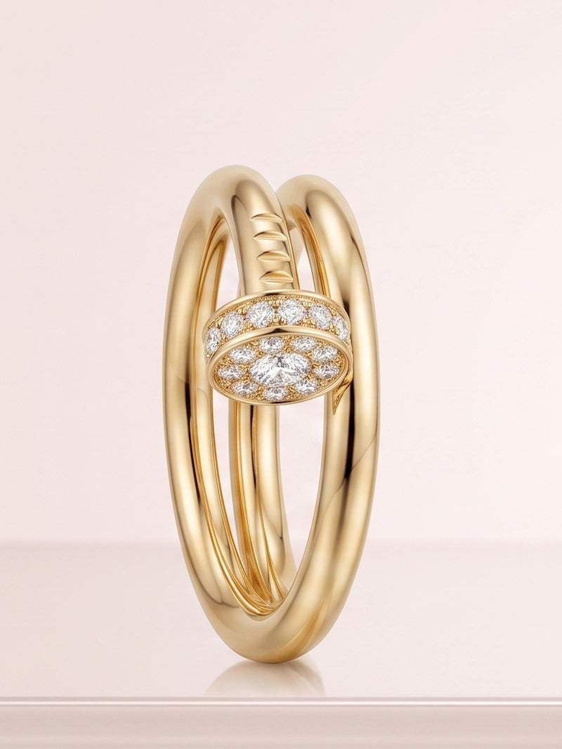 A gold nail ring with a pavé diamond accent band, shown on a soft pink background.