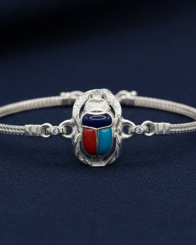 A 925 sterling silver bracelet featuring an Egyptian scarab beetle charm with red, blue, and dark blue inlay, displayed on a gray velvet jewelry cushion.