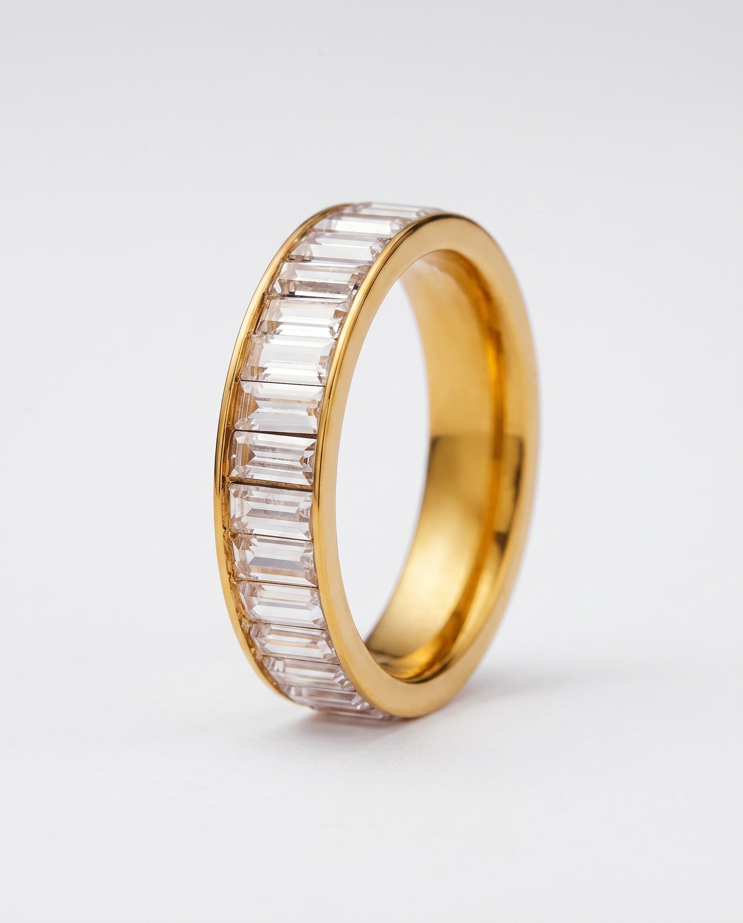 A gold eternity-style ring band with a channel setting of clear baguette-cut stones, shown on a plain white background.