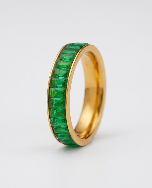 A gold eternity-style ring band with a channel setting of green baguette-cut stones, shown on a plain white background.
