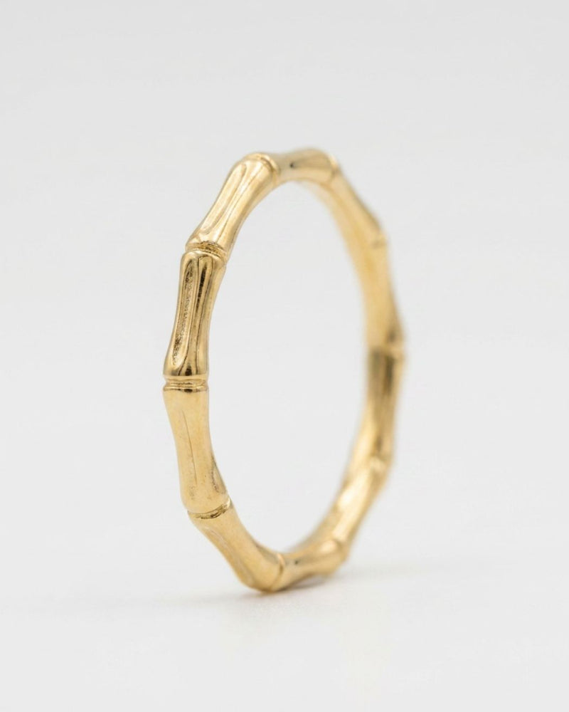 A gold bamboo ring with a textured, segmented design, standing upright on a light gray background.