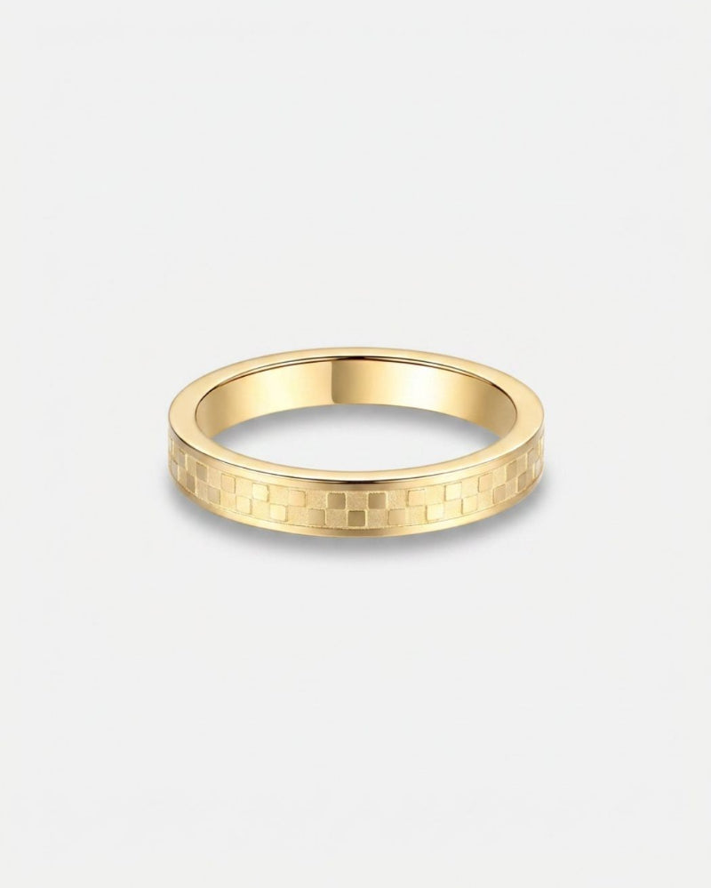 A slim yellow gold band ring with a textured geometric pattern on the outer surface, shown against a light gray background.