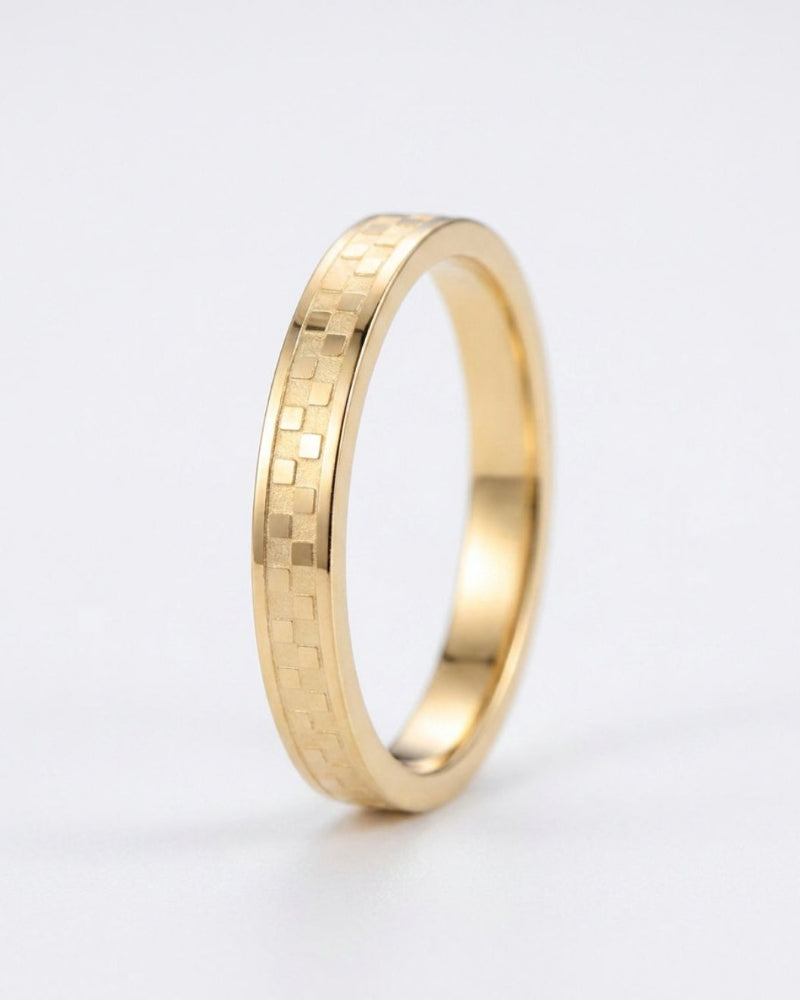 A gold ring with a textured, geometric block pattern on its outer band, shown on a clean white background.