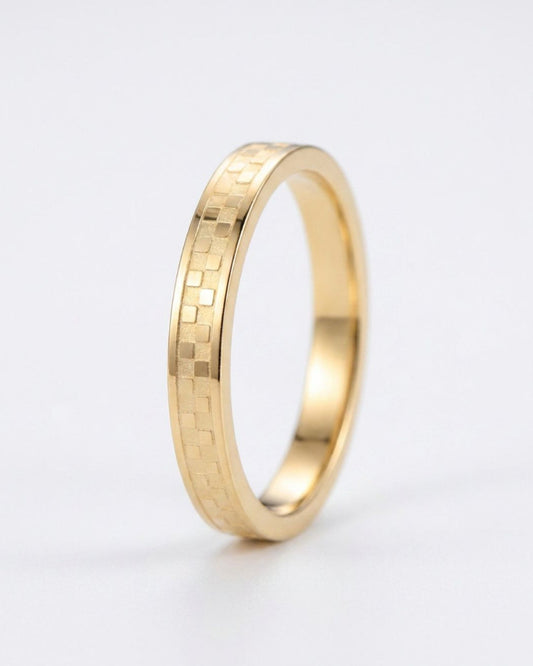 A gold ring with a textured, geometric block pattern on its outer band, shown on a clean white background.