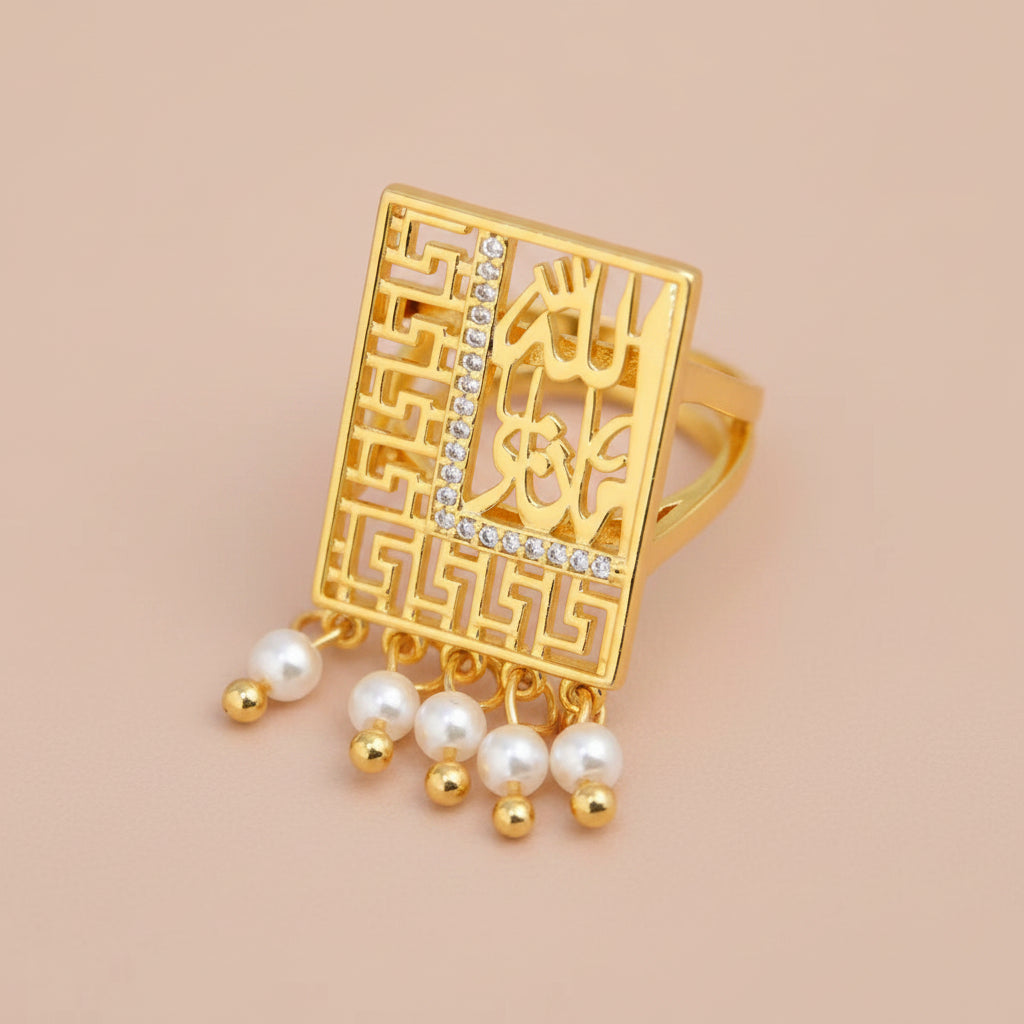 A gold-plated rectangular ring featuring intricate filigree cutouts, geometric border patterns, and dangling pearl beads with small gold beads, set against a soft white satin background.