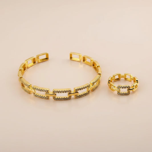 A gold-tone link bracelet and matching ring set, both decorated with rows of small clear stones, displayed on a flat pink surface