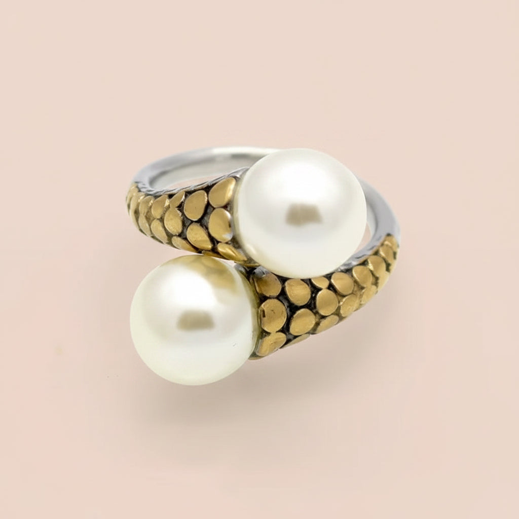 A gold and silver ring featuring two large white pearls, photographed on a clean pink background.