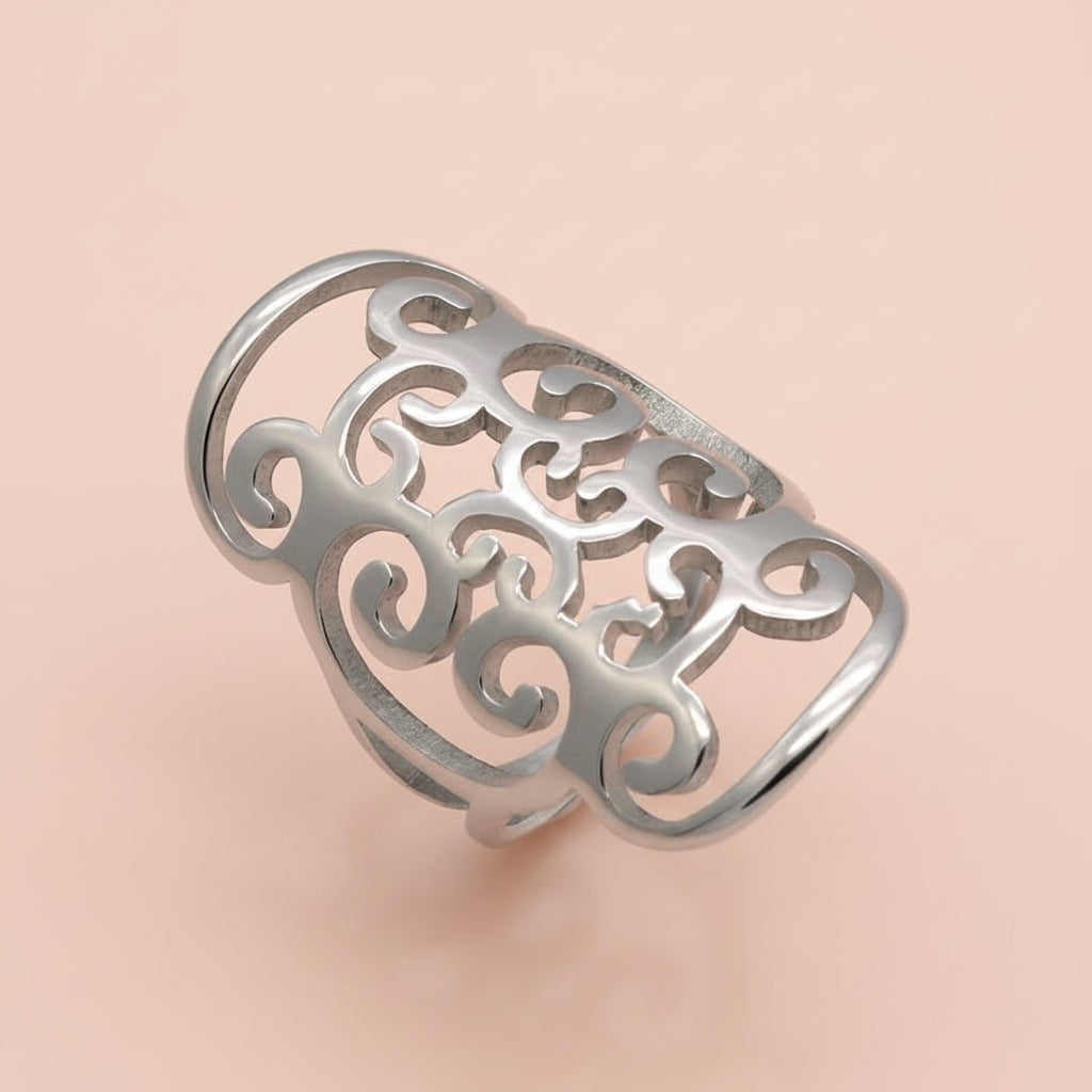 A silver-toned metal ring with an intricate openwork filigree design, photographed on a clean white background with a soft reflection.
