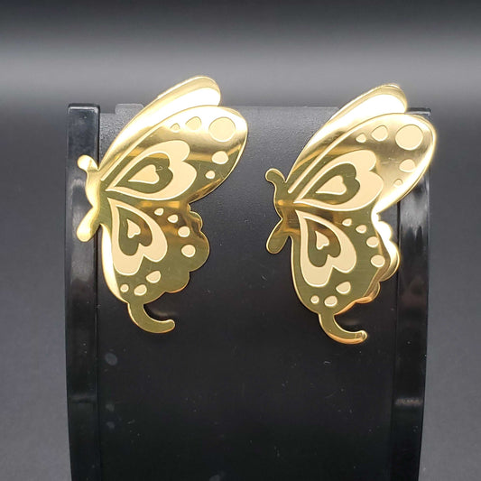 Gold butterfly earrings on a black stand against a dark background