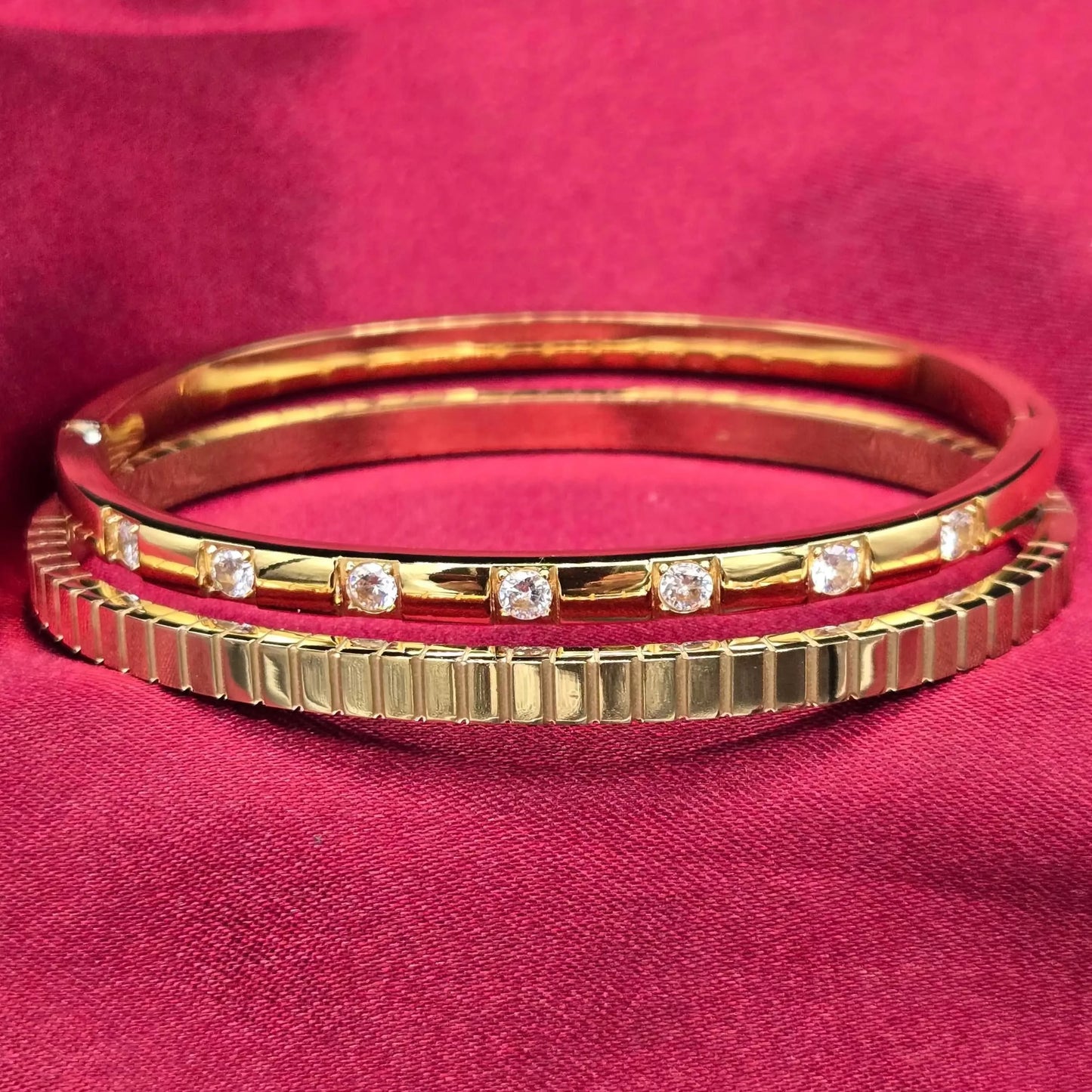 Golden D*ior bangles with diamond accents on a red velvet fabric background