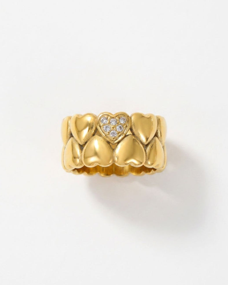 A gold heart-shaped tooth ring with a small heart-shaped cluster of clear stones in the center, displayed on a clean white background.