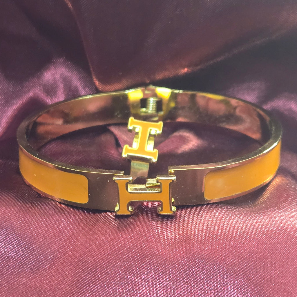 Gold and yellow bracelet with a prominent 'H' logo on a purple fabric background
