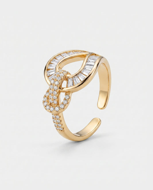 A gold-toned open ring with a knot-like central design, set with clear baguette and round stones, photographed on a light gray background.