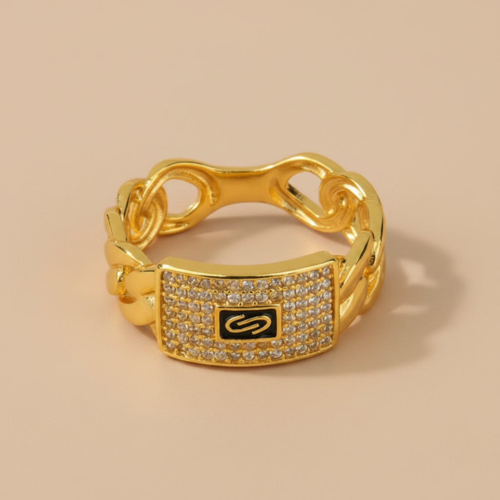 A gold chain-link ring with a rectangular pavé-set centerpiece featuring a black background and a gold infinity symbol, accented with small clear stones.