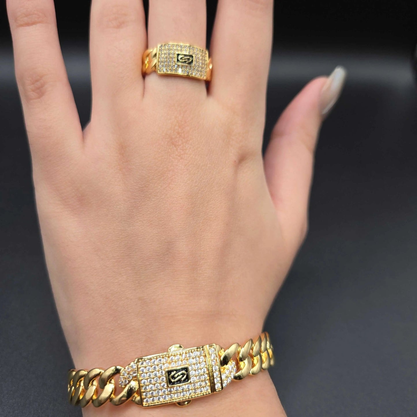 Hand wearing a gold Monaco chain bracelet and ring on a dark background