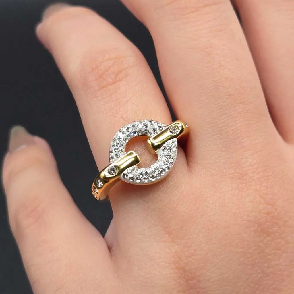 Gold ring with clear stones on a person's finger against a dark background