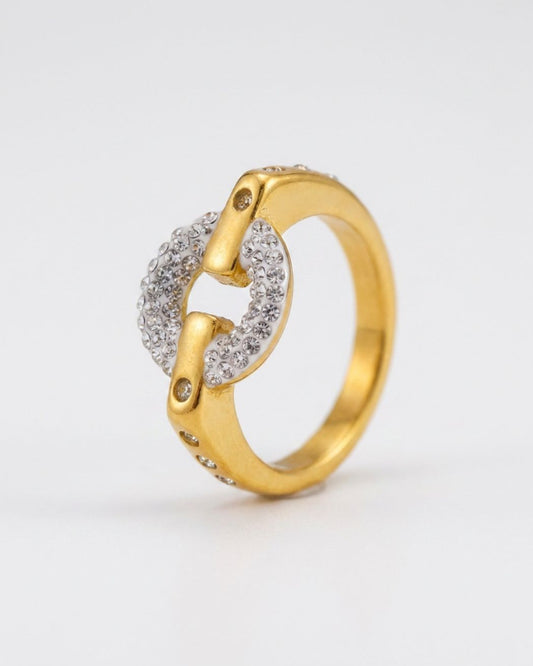 A gold ring featuring a split circular design, with one half paved with small clear stones and the other half accented with tiny gold dots, set against a plain light gray background.