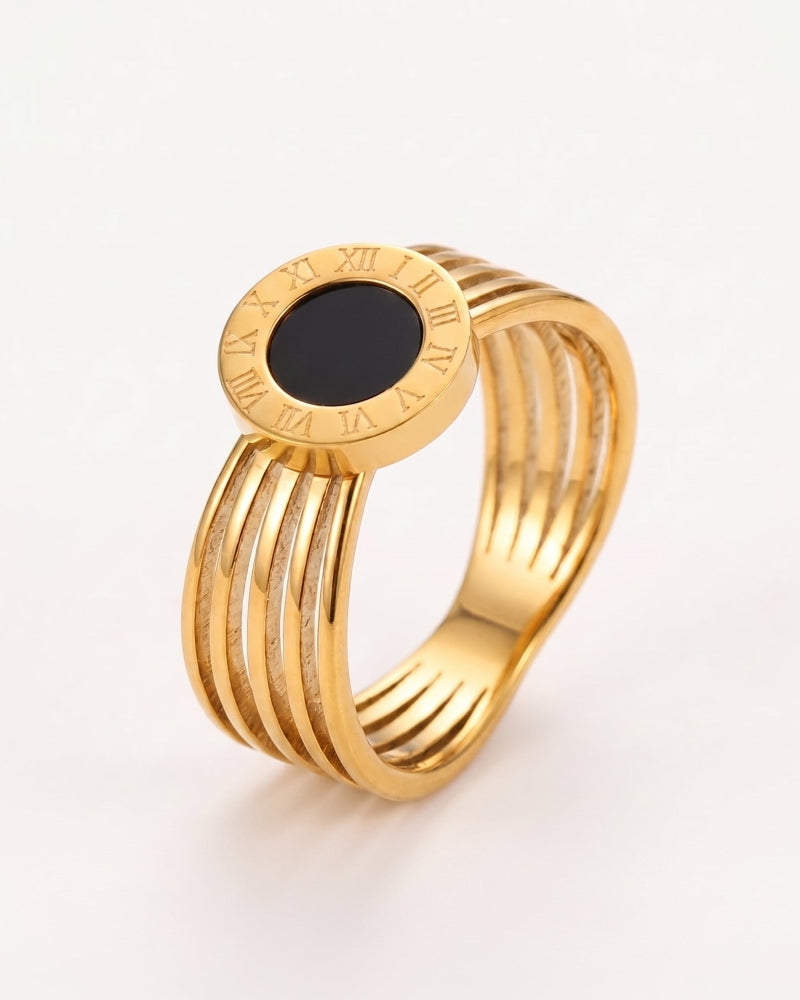 A gold-plated multi-band ring with a central oval black stone and Roman numerals engraved on the top, set against a plain white background.
