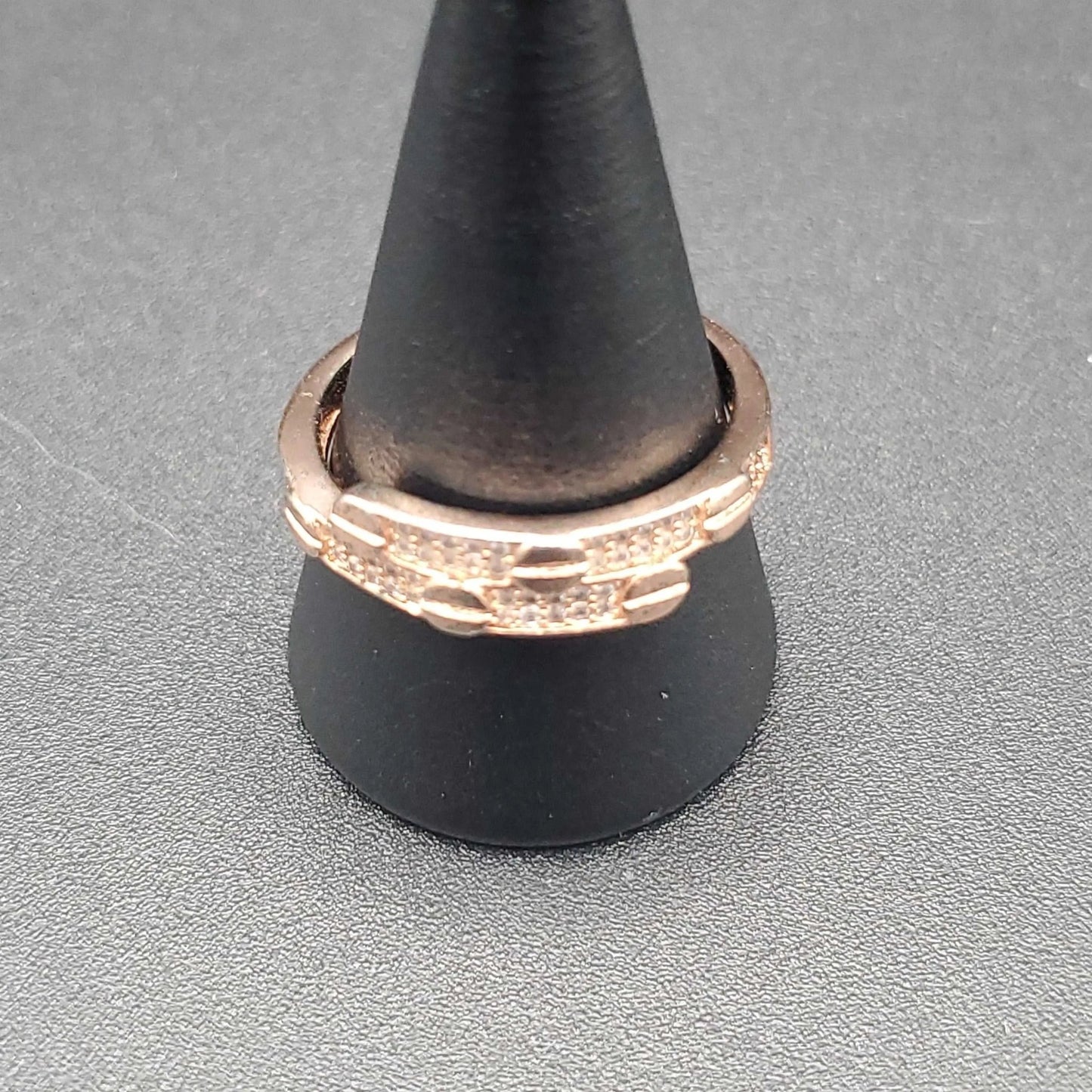 Rose gold ring on a black stand against a gray background