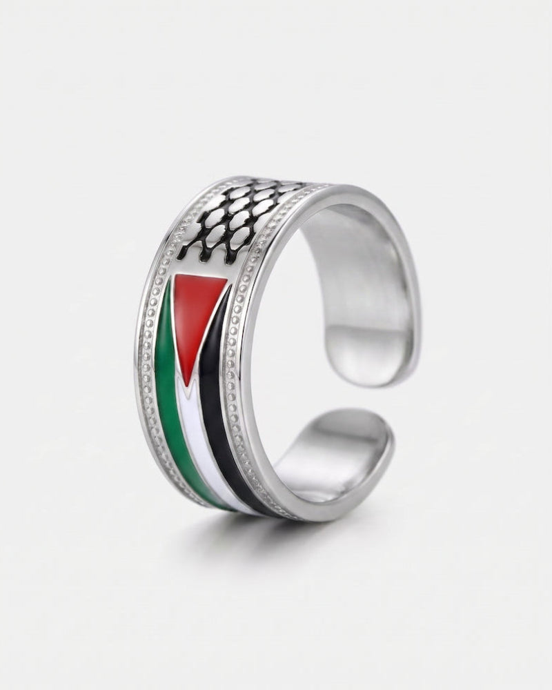 A silver open-band ring featuring an inlaid design of the Palestinian flag (red, white, green, and black) with a black fish-scale pattern on top, set against a plain light gray background.