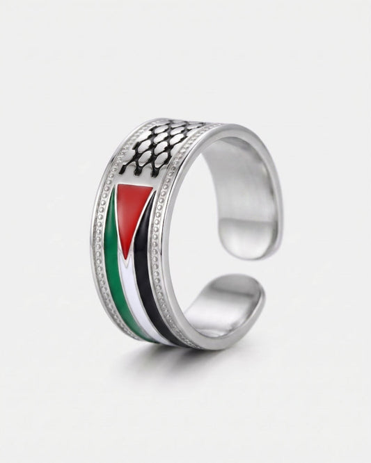 A silver open-band ring featuring an inlaid design of the Palestinian flag (red, white, green, and black) with a black fish-scale pattern on top, set against a plain light gray background.