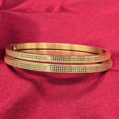 Two golden bangles with a checker design on a red fabric background