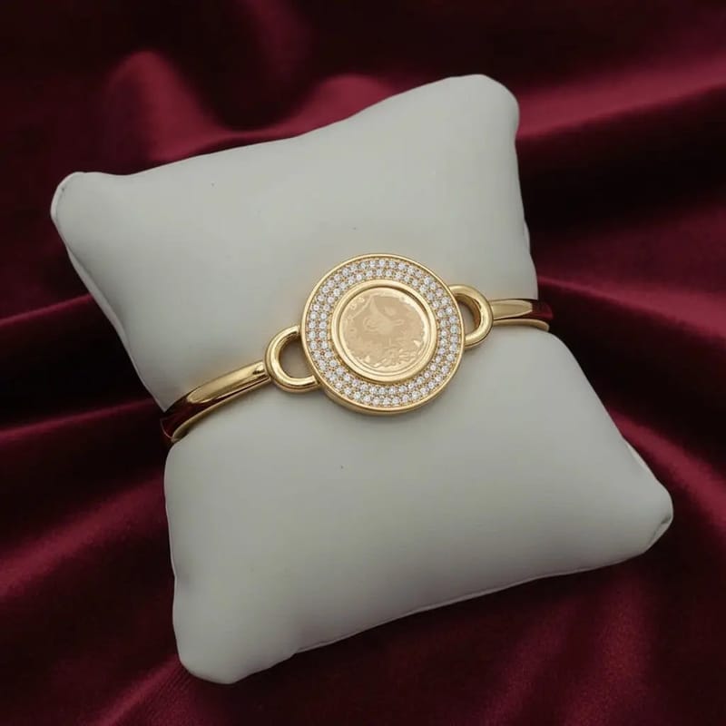 Classic Lira Coin Bangle in Gold finish, with cubic zirconia stone on cluster bangle bracelet on a white cushion