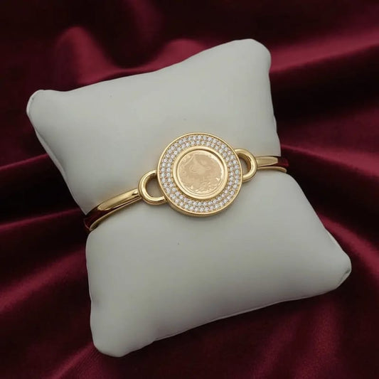 Classic Lira Coin Bangle in Gold finish, with cubic zirconia stone on cluster bangle bracelet on a white cushion
