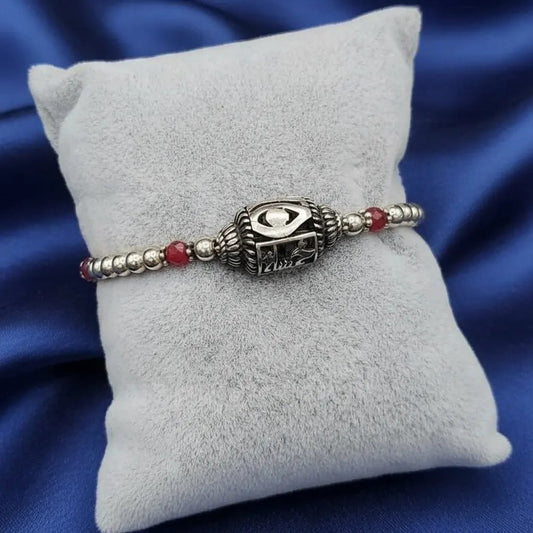 evil eye bracelet made of sterling 925 silver with red beads on a gray cushion against a blue satin background