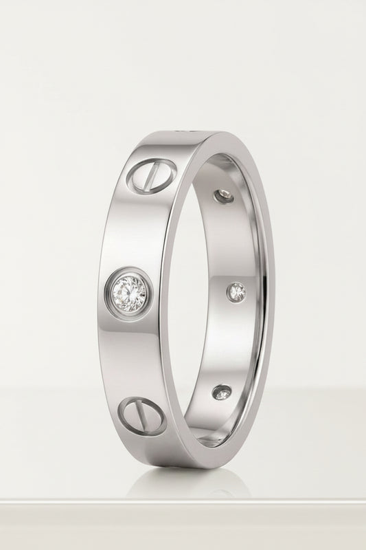 A yellow gold ring with screw details and a round-cut diamond in the center, displayed on a light pink background. Cartier Love Design