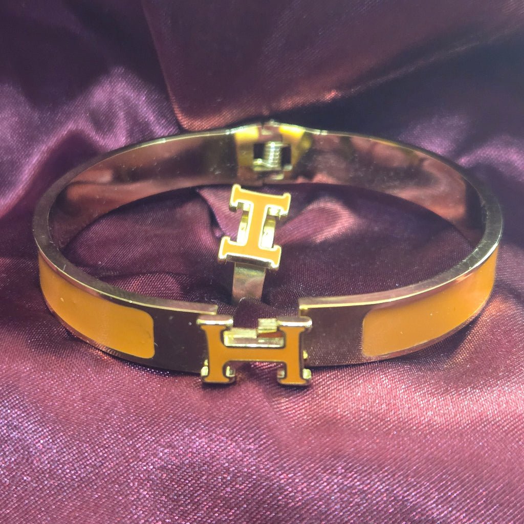 H-Signature Bangle Set in Gold finish on a dark purple background