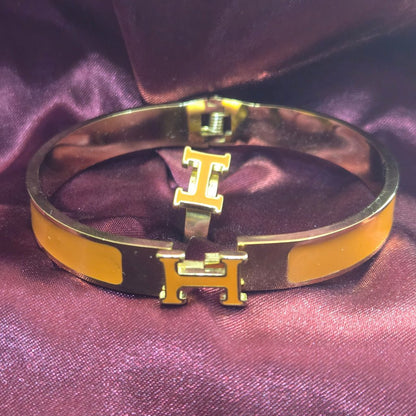 H-Signature Bangle Set in Gold finish on a dark purple background