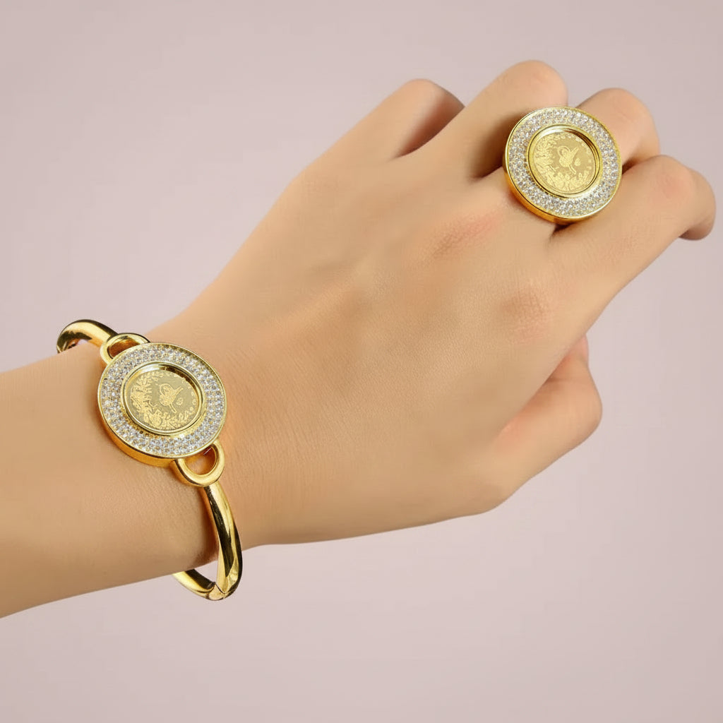 A gold-plated bangle bracelet and matching ring set, both featuring a central gold coin-like medallion surrounded by clear rhinestones, shown worn on a hand against a black background.