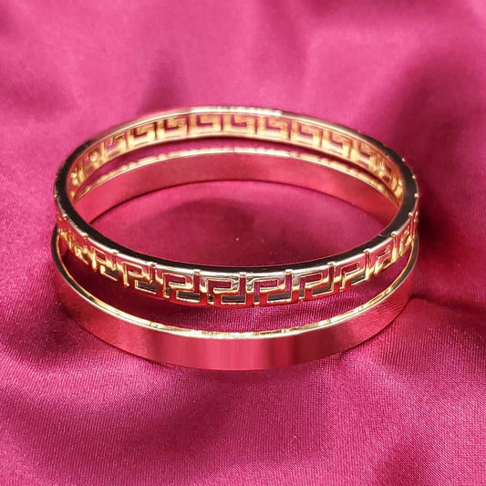 Modern Greek Key Bangle in Gold finish on a red fabric background