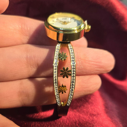 Gold watch and floral-patterned bracelet on a hand against a red fabric background