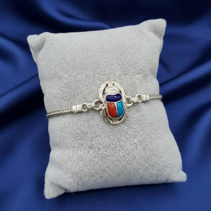 Silver bracelet with a colorful Scarab charm on a gray pillow against a blue satin background