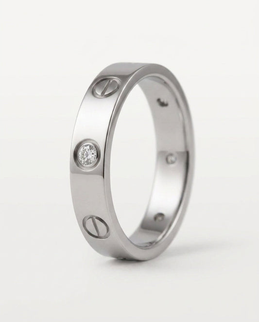 A silver-toned screw-ring band ring with three screw details and one clear gemstone, shown on a light gray background.