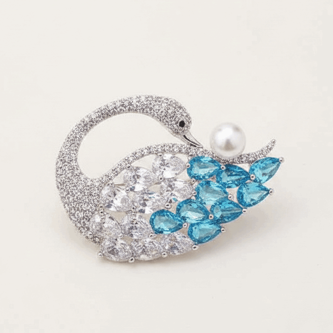 Decorative swan brooch with blue stones and a pearl on a light gray background