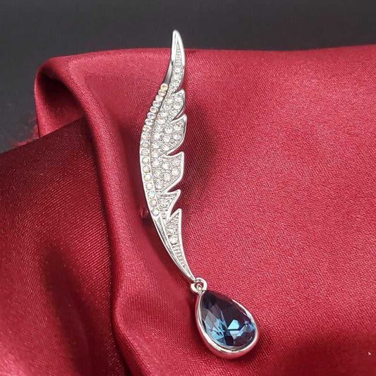 Timeless Feather Brooch in Silver finish, with cubic zirconia stone on and a blue pear-shaped stone